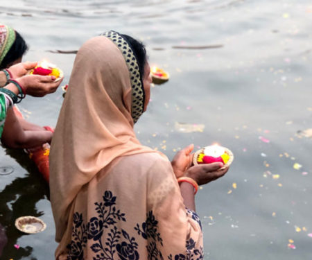 Foto di una donna con vestito tradizionale che sull'acqua compie un rituale con una candela.